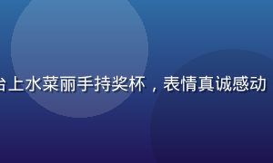 水菜丽获奖典礼现场，颁奖台上水菜丽手持奖杯，表情真诚感动，灯光聚焦于她的标志性笑容